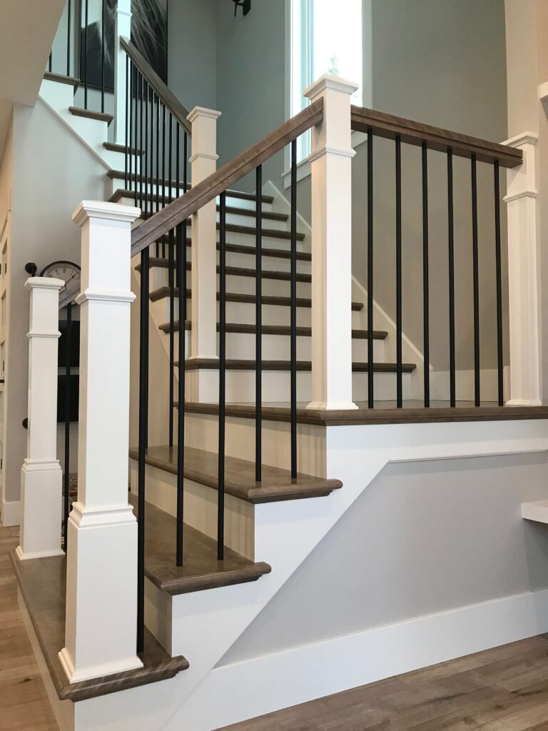 Custom hardwood staircase with black metal balusters, white newel posts, and stained oak treads in a modern Moncton home