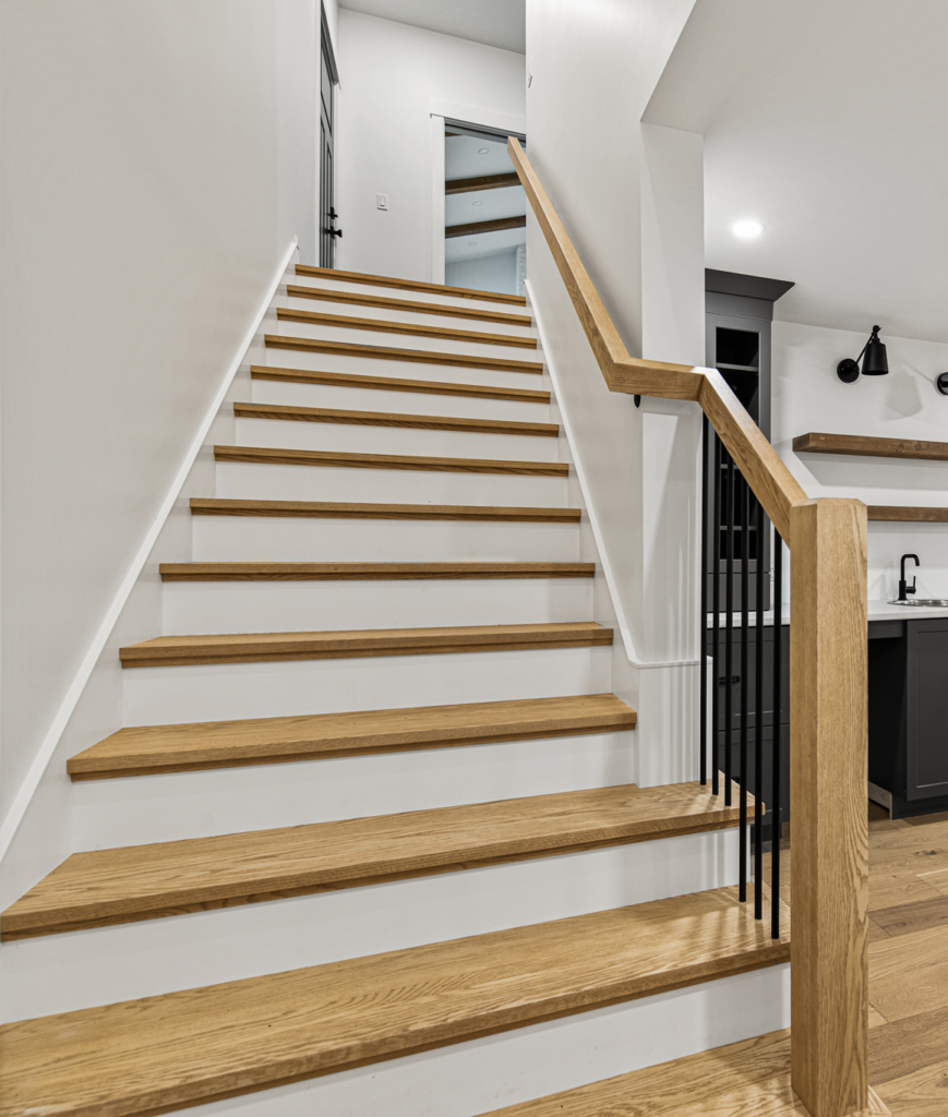 Custom white oak staircase with white risers, black metal spindles, and solid oak handrail in a modern Moncton home